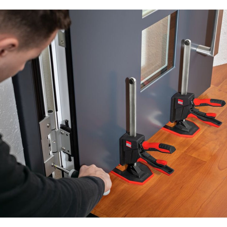 Person using two Bessey Tools Beyceps to lift and level a door while he attaches the hinges with screws