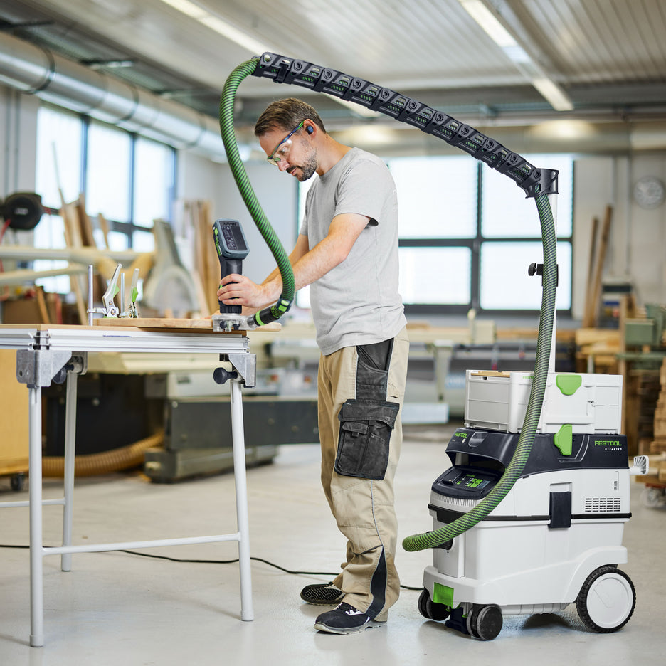 Woodworker used a cordless trim router to profile the edge of a round wooden workpiece while the router's hose is suspended overhead by the Boom Arm on top of a CT 36 dust extractor.
