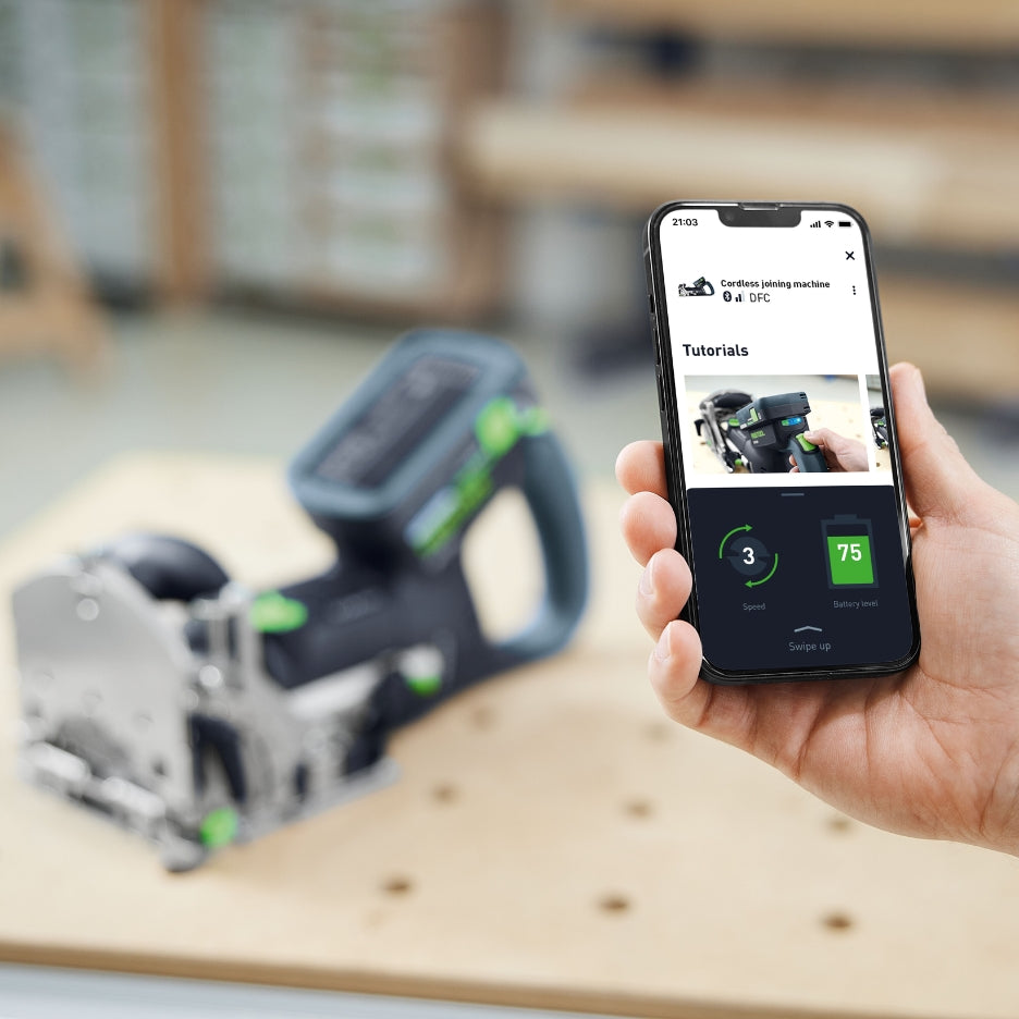 Hand holding a smartphone using Festool app with Festool Cordless Domino Joiner DFC 500 blurred on the background