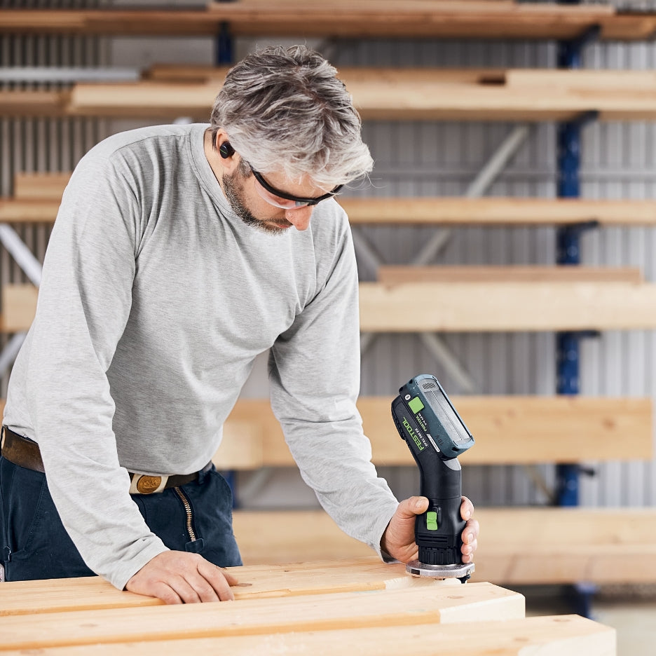 Man using Festool Cordless Edge Trimming Router OFKC 500 R3 EB-Basic on wooden planks in a workshop setting