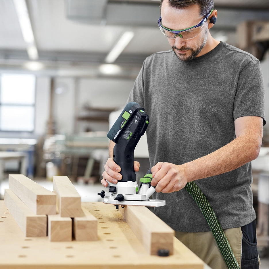 A person using the Festool MFKC 700 EB router to cut a groove or rebate along the edge of a wooden board in a shop environment