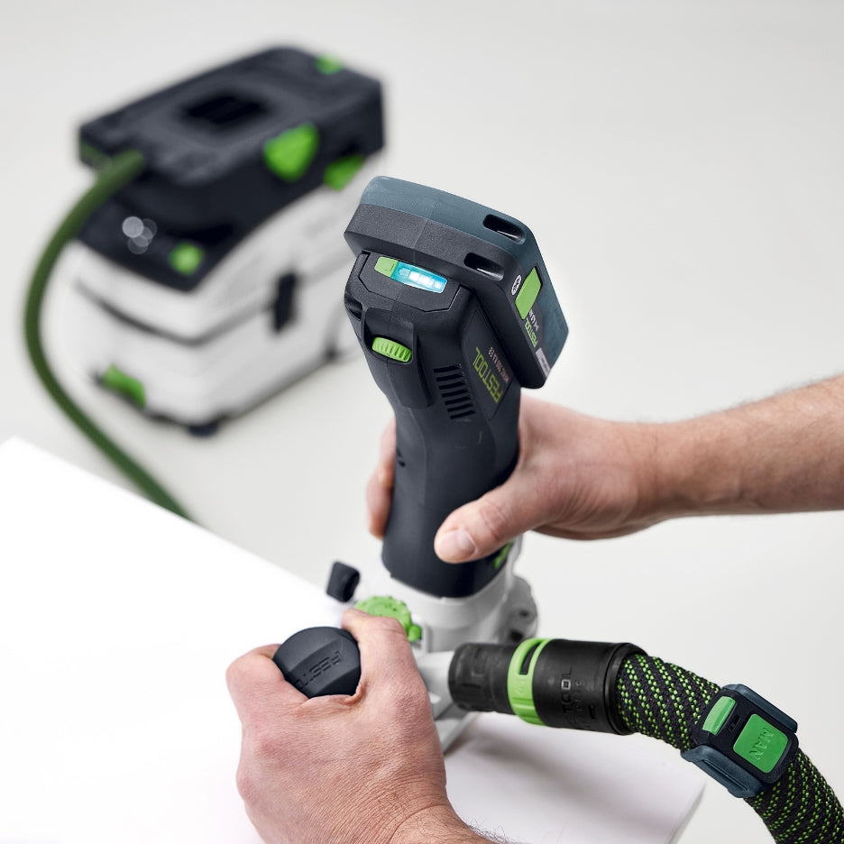 A close-up view showing a person using the Festool MFKC 700 EB-Basic edge trimming router to flush trim the edge of a workpiece with a dust extraction hose attached