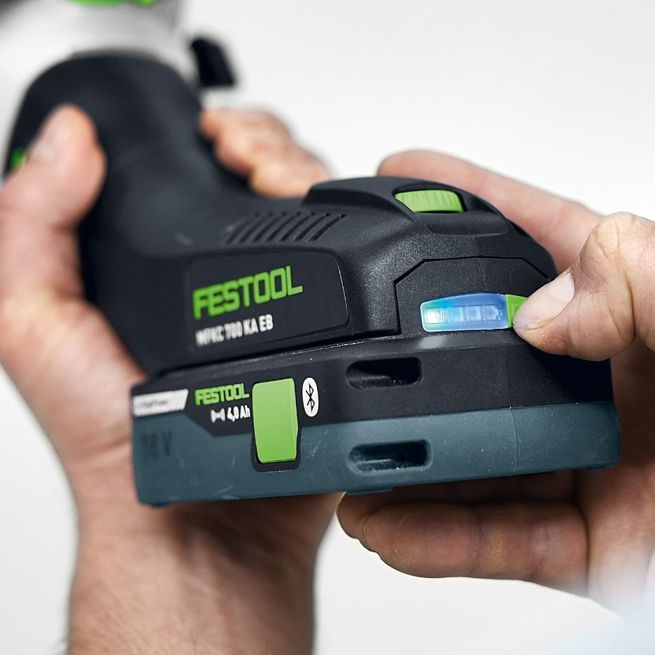 Close-up shot of a person’s hand holding a Festool 18V battery pack attached to the MFKC 700 EB router, showing the LED charge level indicator