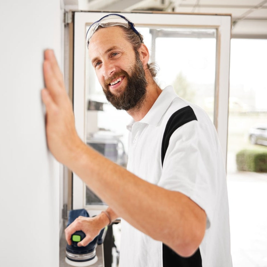 Man holding Festool ETSC 2 125 in one hand and checking wall smoothness with the other