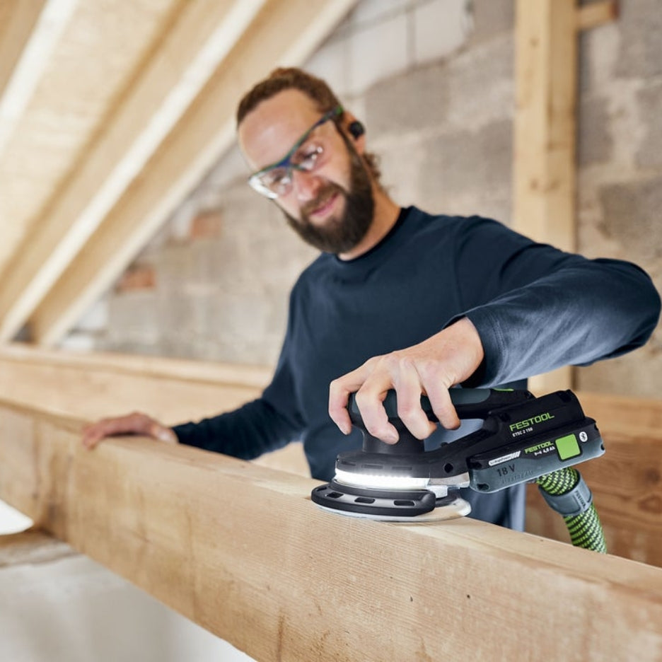 Man sanding a wooden beam using Festool ETSC 2 150 with integrated LED light, inside building