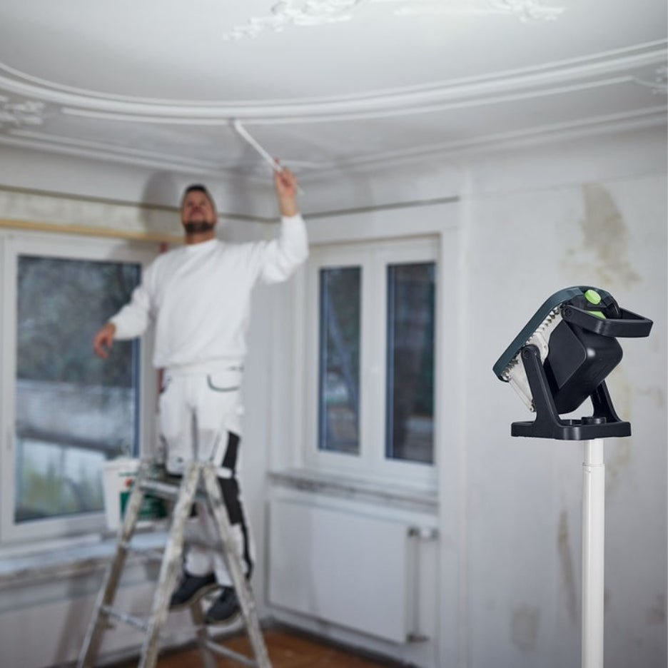 Festool Cordless Site Light SYSLITE KBS C on pole, illuminating man painting the ceiling
