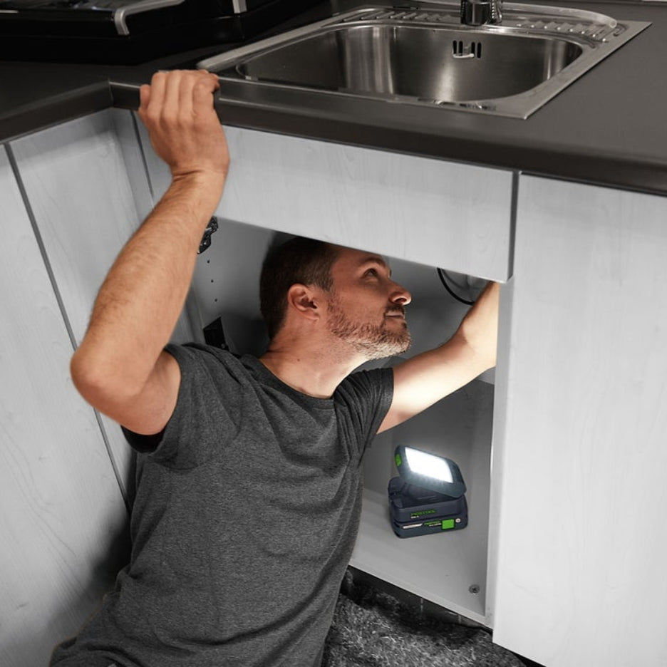 Man fixing under the sink and using Festool Cordless Task Light SYSLITE KAL C to illuminate area