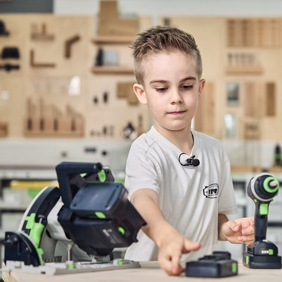 Boy reaches for a battery for his toy Festool cordless track saw.