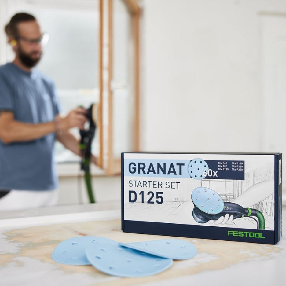 Box of Festool Granat 5 Inch Abrasive Assortment D125 GR-Set and man sanding in the backgrund