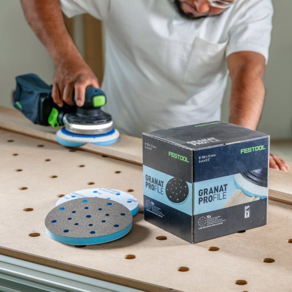 Man sanding a piece of wood using a Festool sander and Festool Grit Abrasives Granat PROfile D150 M GR PRO and box of Man sanding a piece of wood using a Festool sander and Festool Grit Abrasives Granat PROfile D150 M GR PRO on top of MFT table