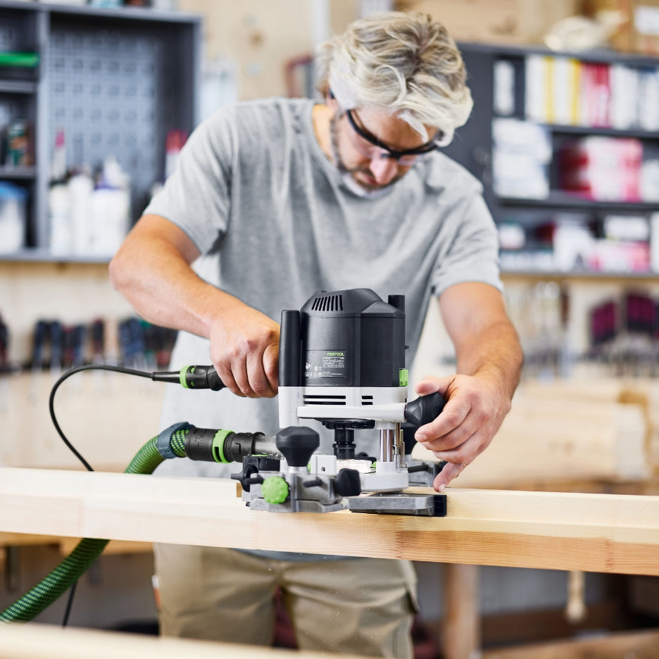 Man using Festool Plunge Router OF 1400 EQ-F-Plus on a wooden workbench in a workshop.
