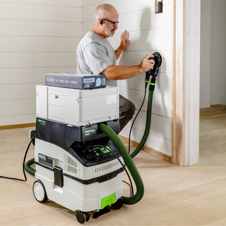 Man using ETS EC 150/5 Plus Random Orbit Sander attached to CT MIDI I HEPA Dust Extractor with Systainer and D150 GR-Set Granat Starter Set box on top.