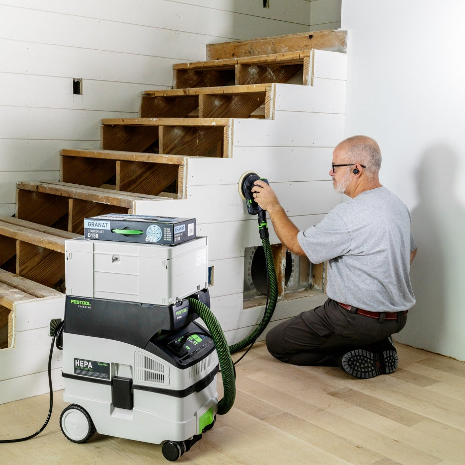Man sanding with ETS EC 150/5 Plus Random Orbit Sander attached to CT MIDI I HEPA Dust Extractor with Systainer and D150 GR-Set Granat Starter Set box on top.
