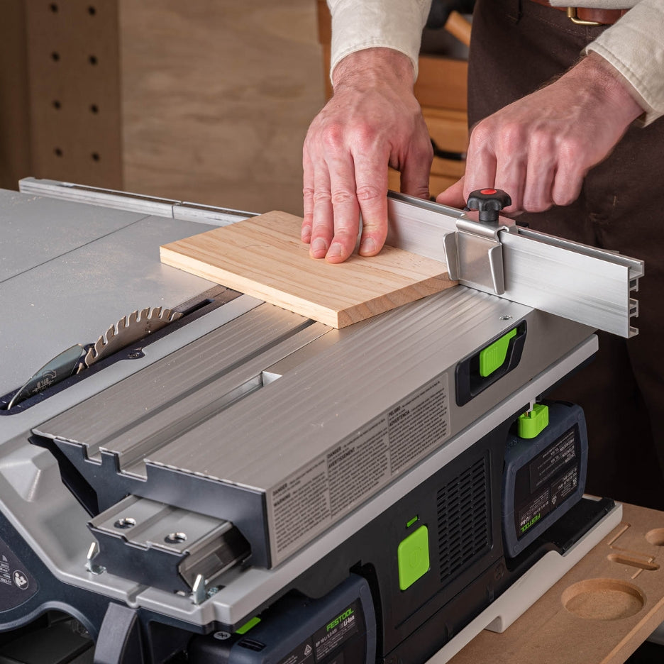Person guiding a small wood panel through the Festool CSC SYS 50 table saw, using the TSO Extended Miter Fence with a stop block for precise cutting.