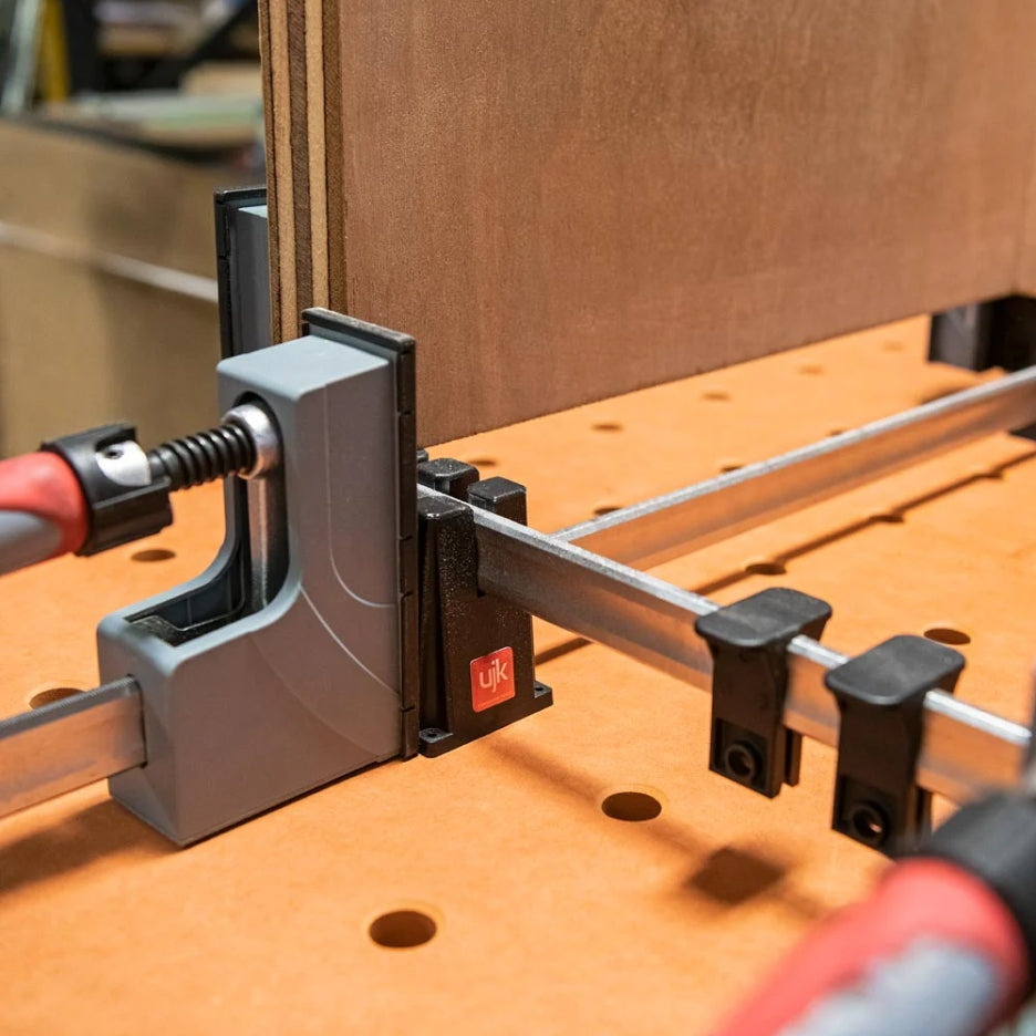 Woodworking clamp attached to UJK Tools Clamp Stand on a wooden surface with a blurred background