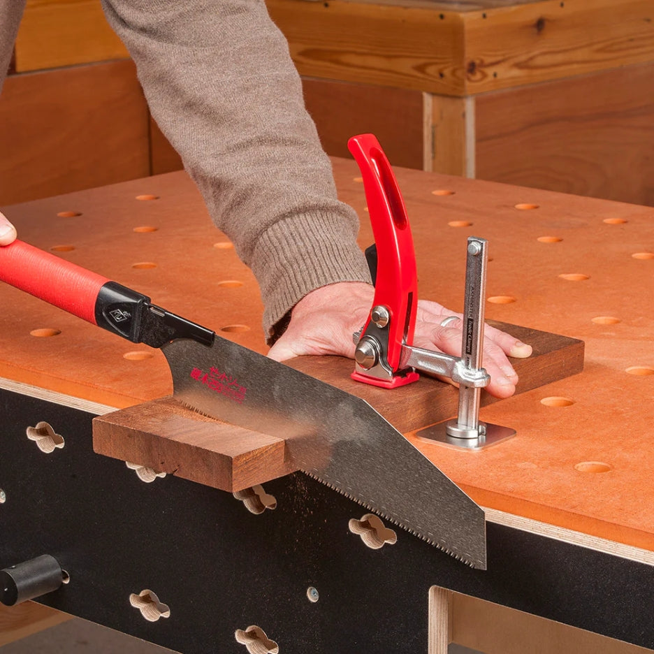 Person using a saw to cut a piece of wood on a workbench and UJK Tools HDF Valchromat Top for Parf Dogs with a clamp holding it in place.