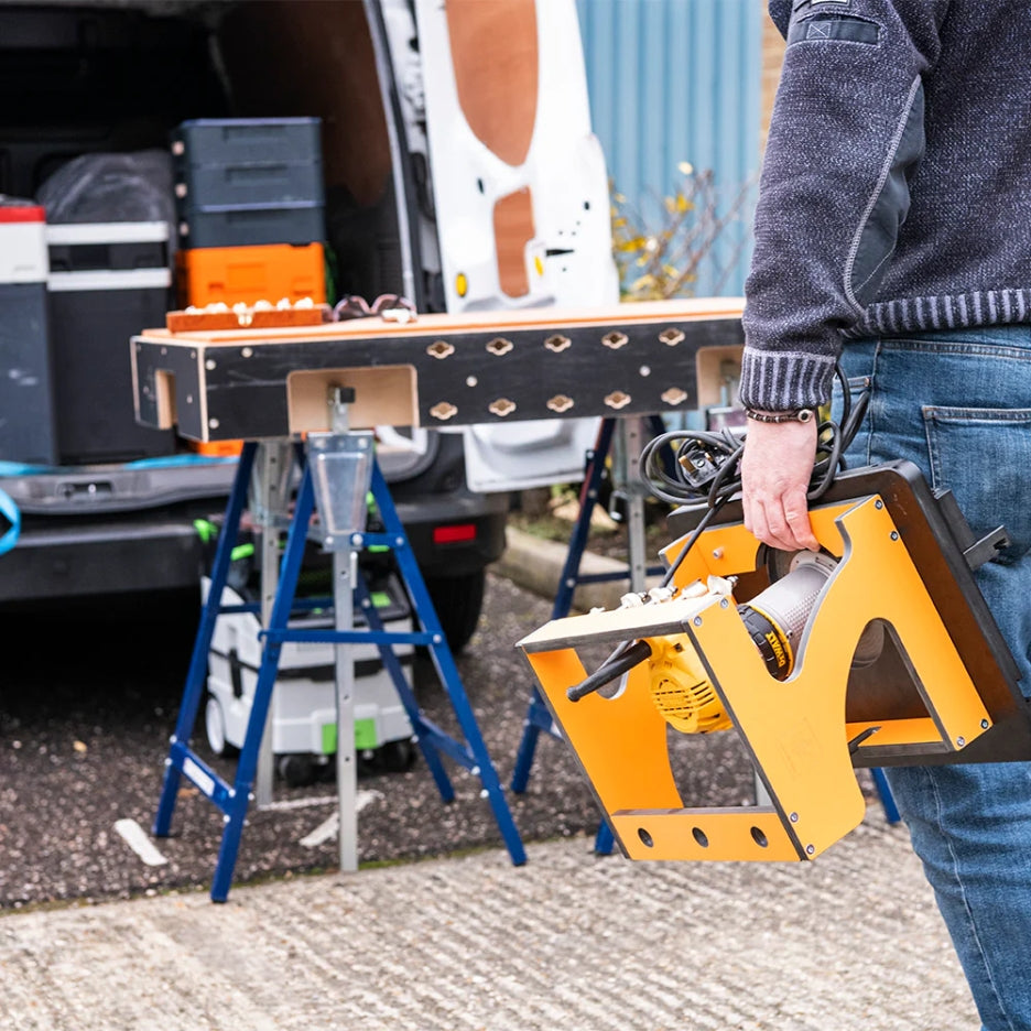 Person holding UJK Tools Portable Trim Router Table next to a workbench with a van in the background