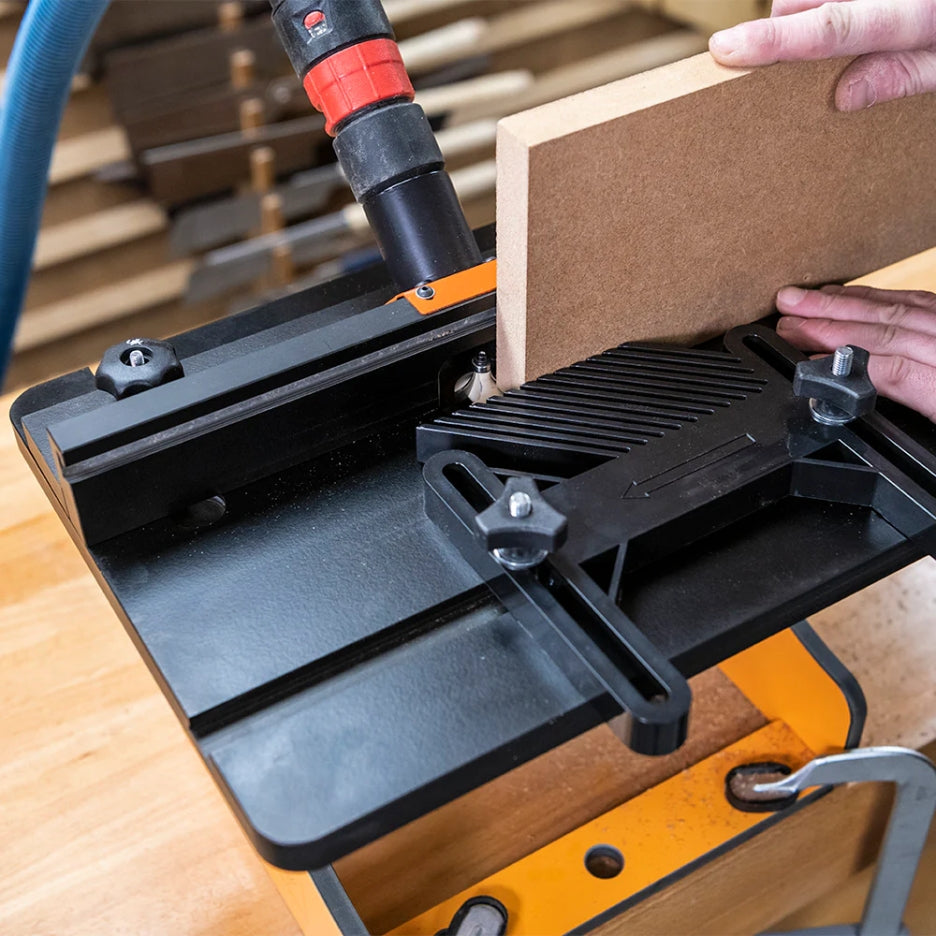 UJK Tools Portable Trim Router Table with a piece of wood being cut, with a person's hand holding the wood steady.