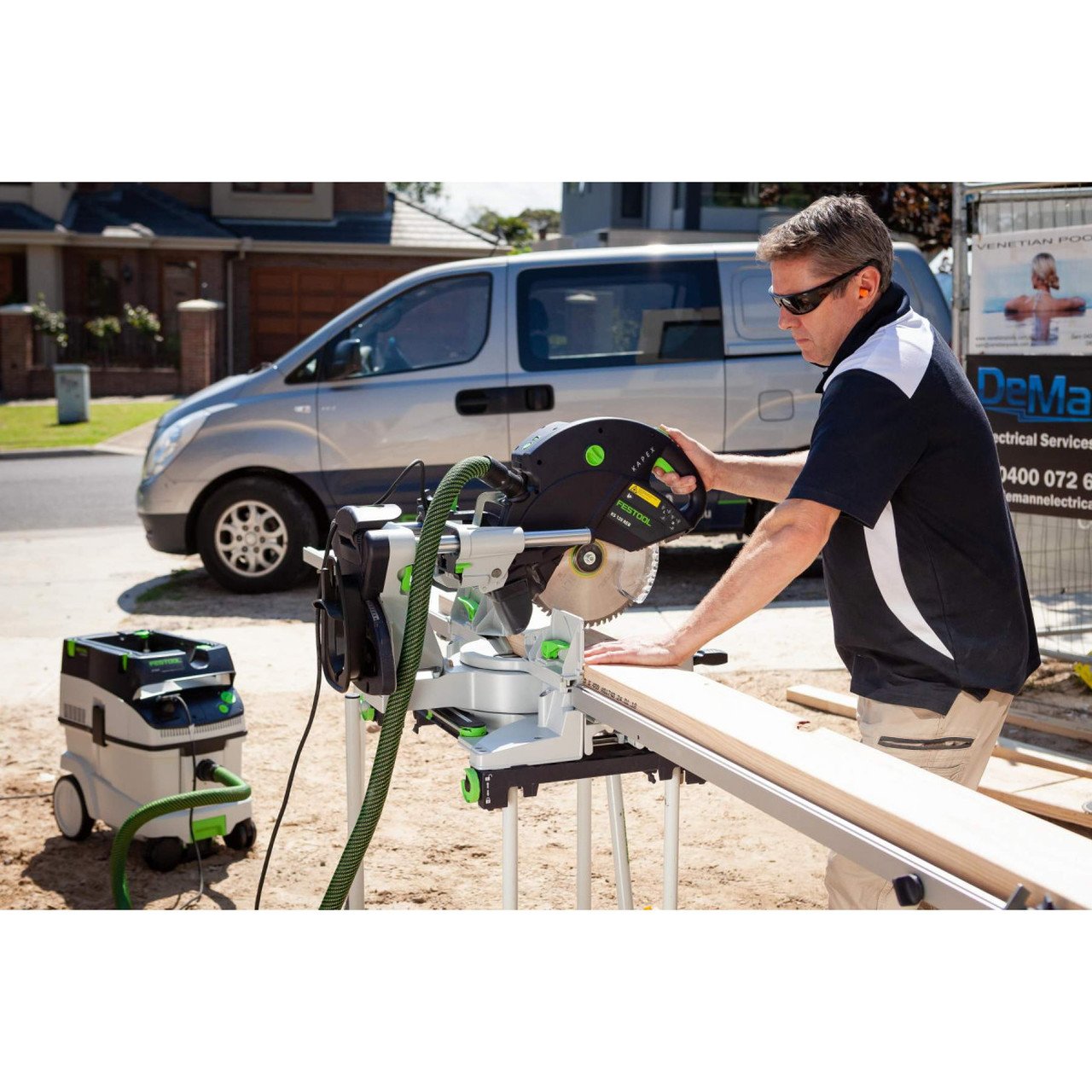 A contractor prepares to cut a 2x8 on the Kapex outdoors on a construction site. Saw is on stand with wings attached.