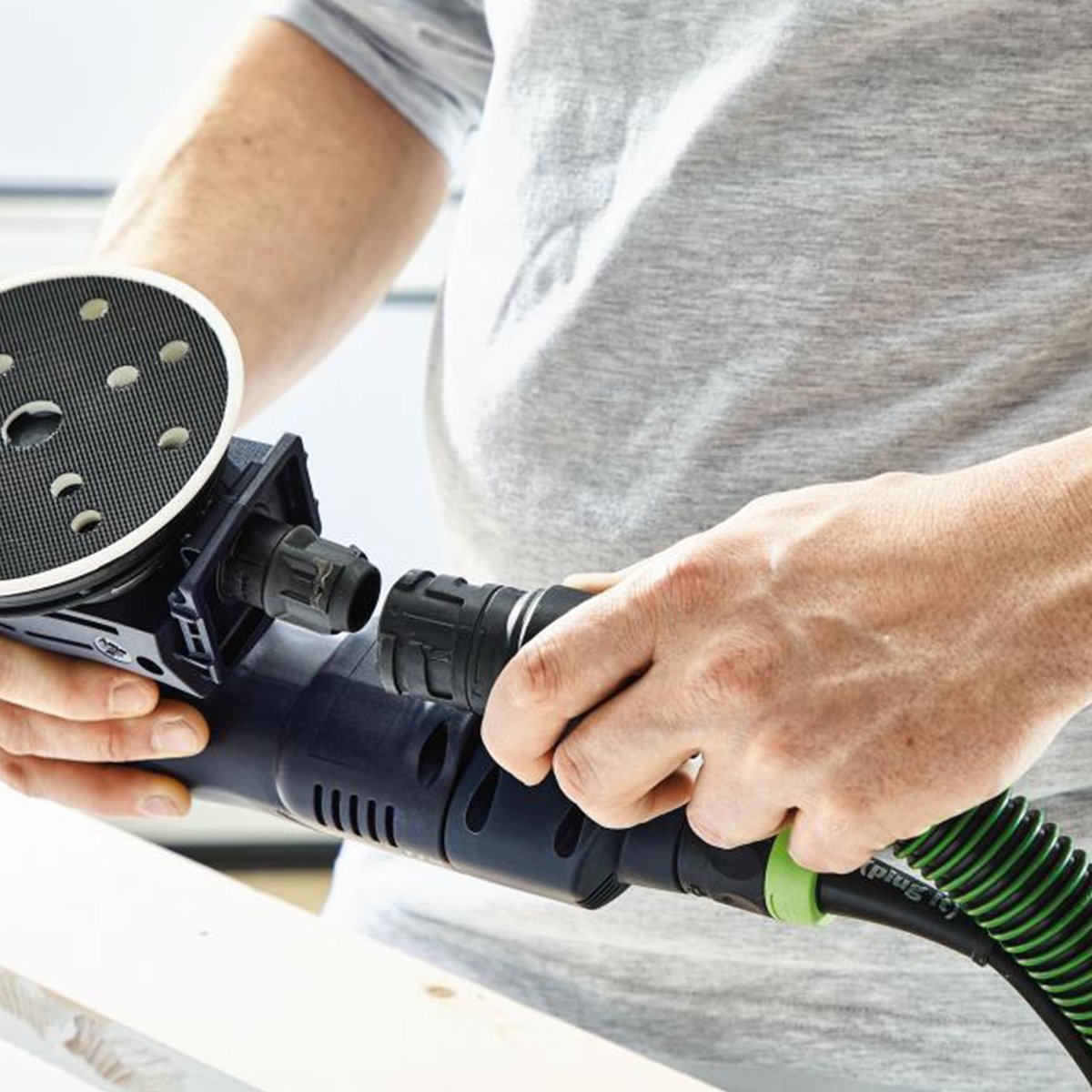 The dust bag is removed and an operator is attaching a dust extractor hose to the ETSC sander.
