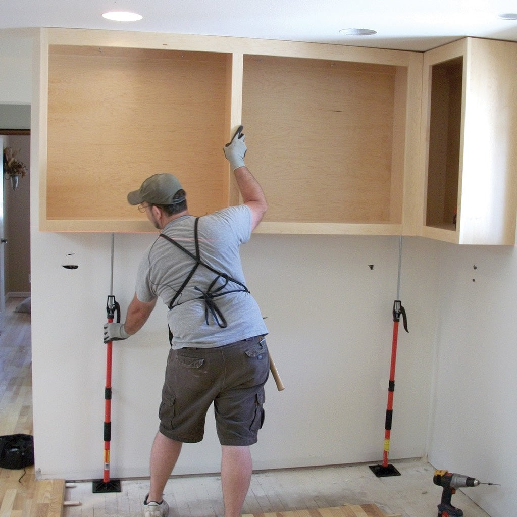 A worker uses 2 Upper Hands to support and position a large L-shaped cabinet so he can fasten it to the wall.
