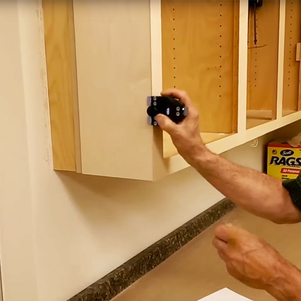 A worker uses the Tri Trimmer to trim edge banding flush down the side of the cabinet.