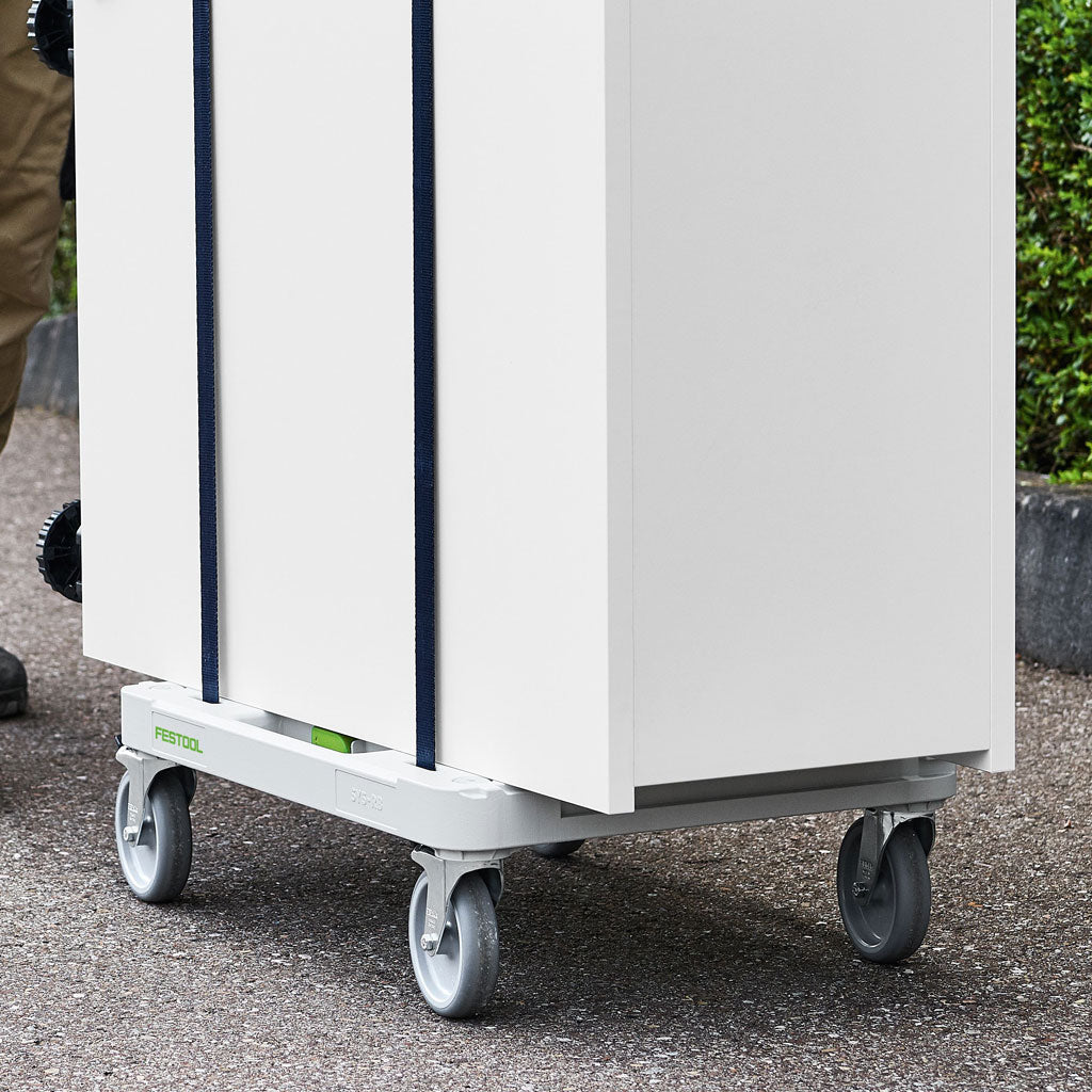 A worker pushes a large cabinet across pavement. The cabinet is strapped to the Sys-Cart through the frame.