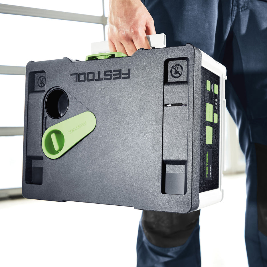 Man carries CTC SYS Cordless Dust Extractor by folding front handle. Pivoting closure seals compartment.