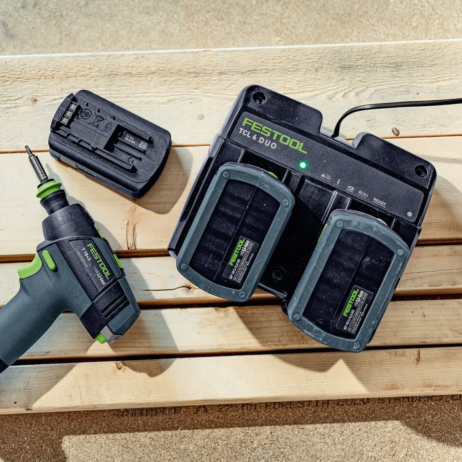 Festool TCL 6 DUO battery charger with two batteries on a construction site with a drill.