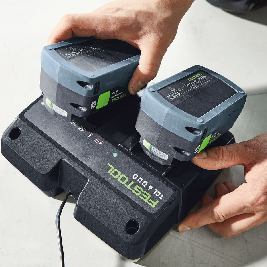 A worker slides on two Festool Bluetooth batteries for charging.