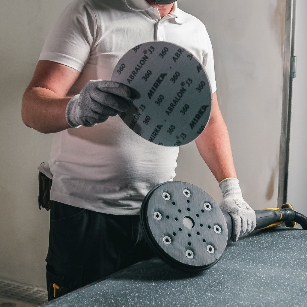 An operator installs a Mirka Abralon foam-backed sanding pad on the interface pad of his Mirka LEROS 9" random orbit sander.