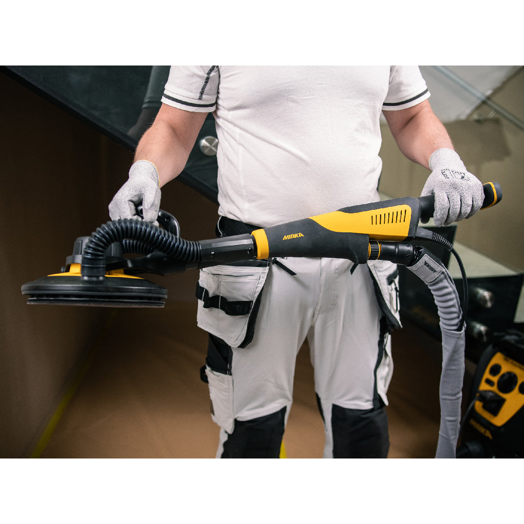 A drywaller holds the LEROS-S across his body in his hands, providing scale. Connected to dust extractor with hose.