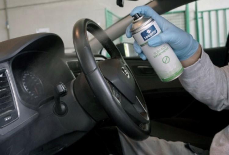 A worker sprays Sanius on the steering wheel of a car.