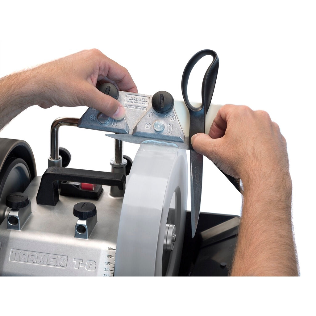 A man uses the Tormek SVX-150 Scissor jig to sharpen the bevel of a pair of scissors on a wet wheel.
