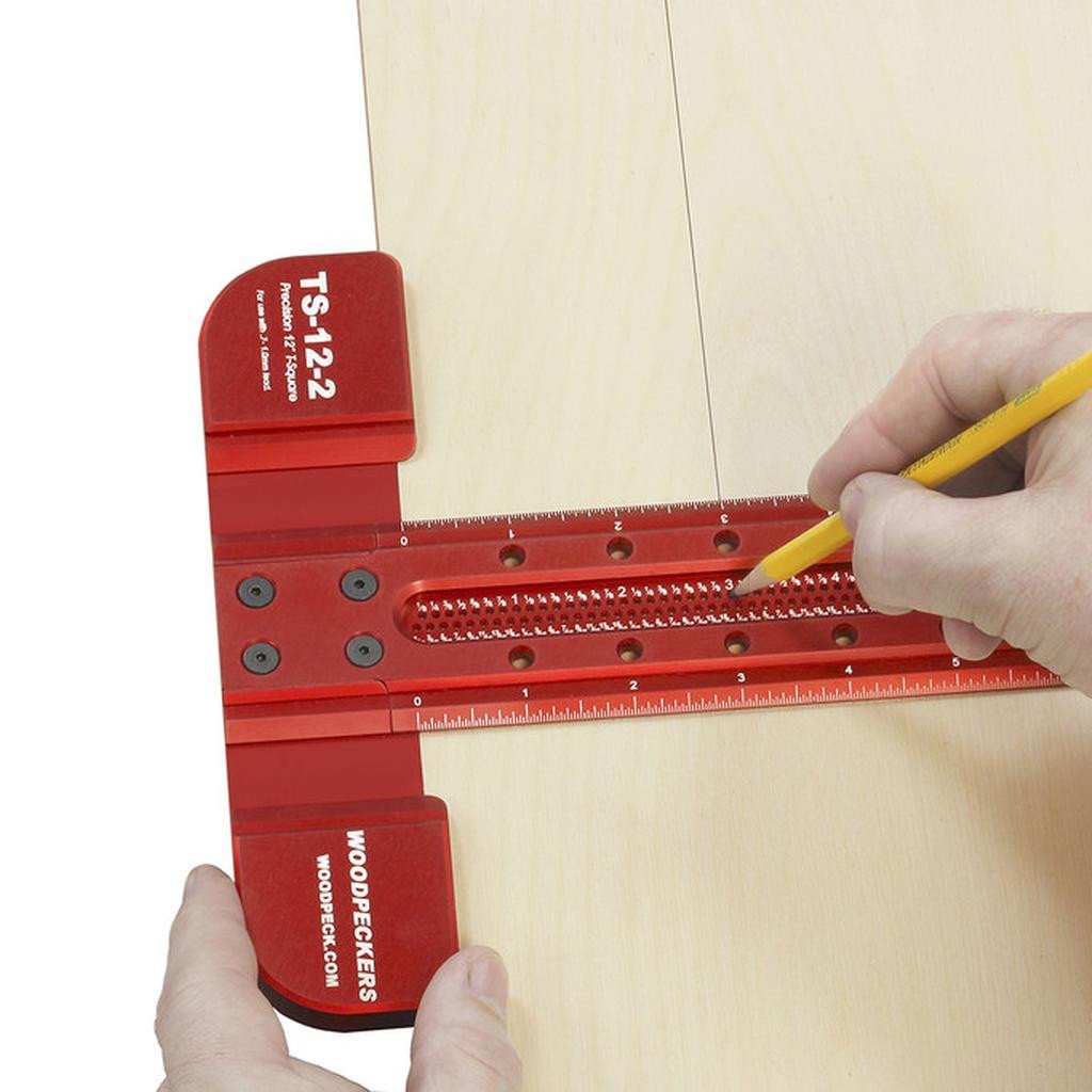 A woodworkers has placed a pencil in a hole and pulls the 12" T-square along the edge of plywood to draw a parallel line.
