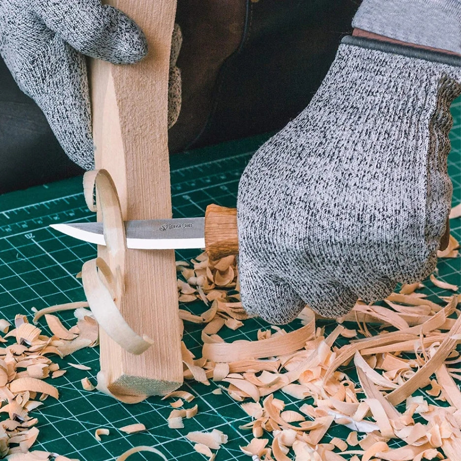Person using a BeaverCraft knife to carve wood on a green cutting mat with wood shavings.