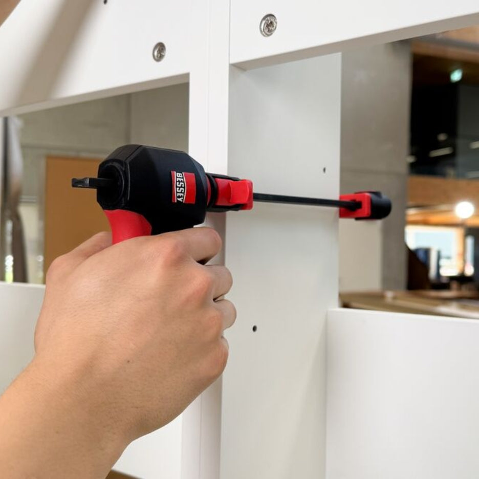 Hand using Bessey Tools Trigger Clamps on white wood.