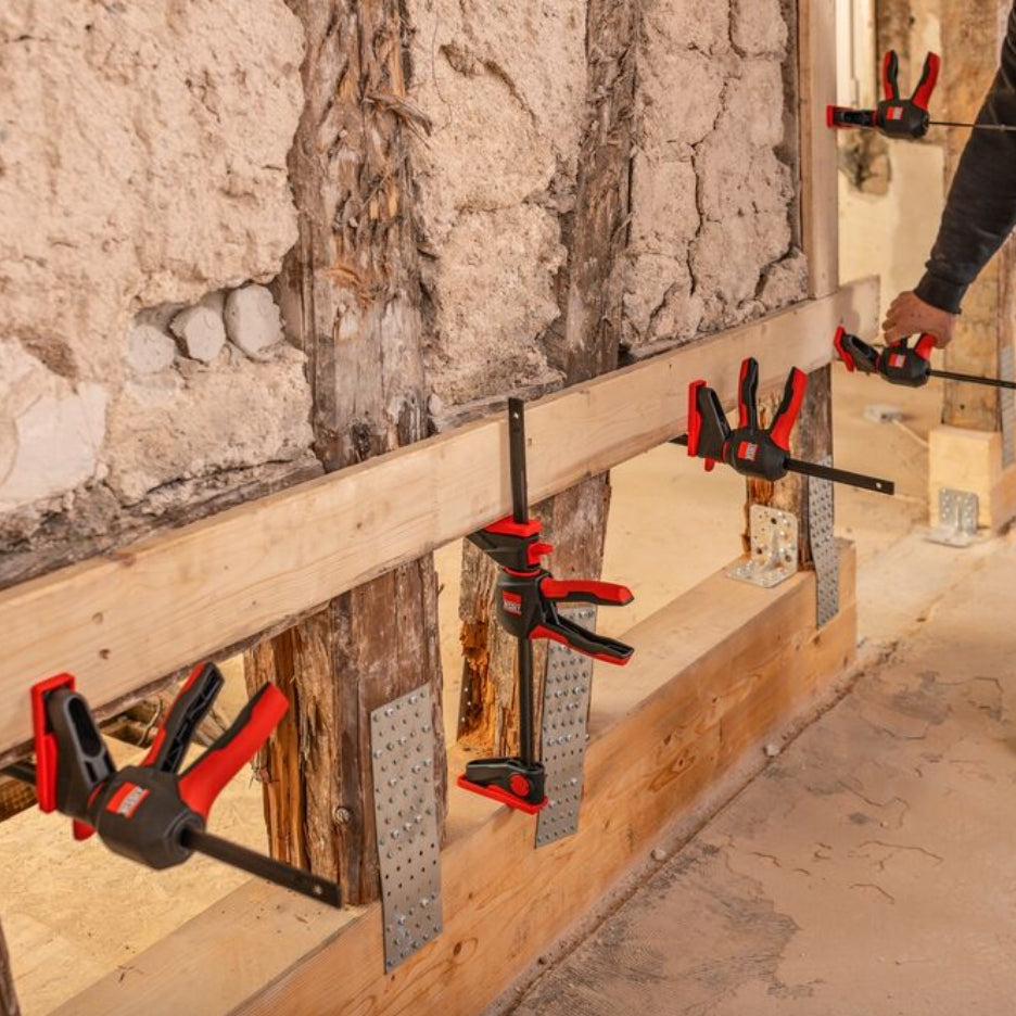 Wooden beams secured with Bessey Tools Trigger Clamps against a wall.