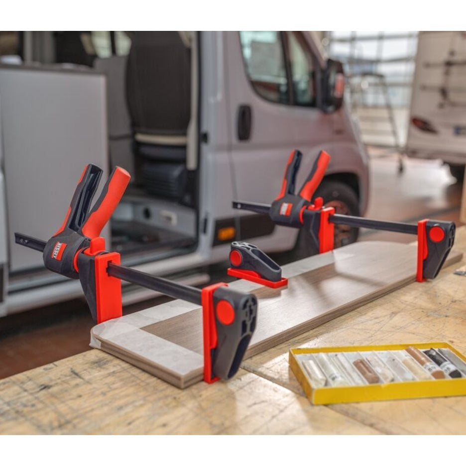 Bessey Tools Trigger Clamps holding a wooden panel on a workbench with a van in the background