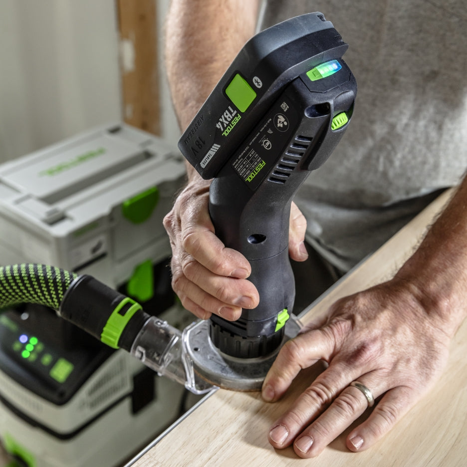 Person using Festool Cordless Edge Trimming Router OFKC 500 R3 EB-Basic on a wooden surface with a workshop background.
