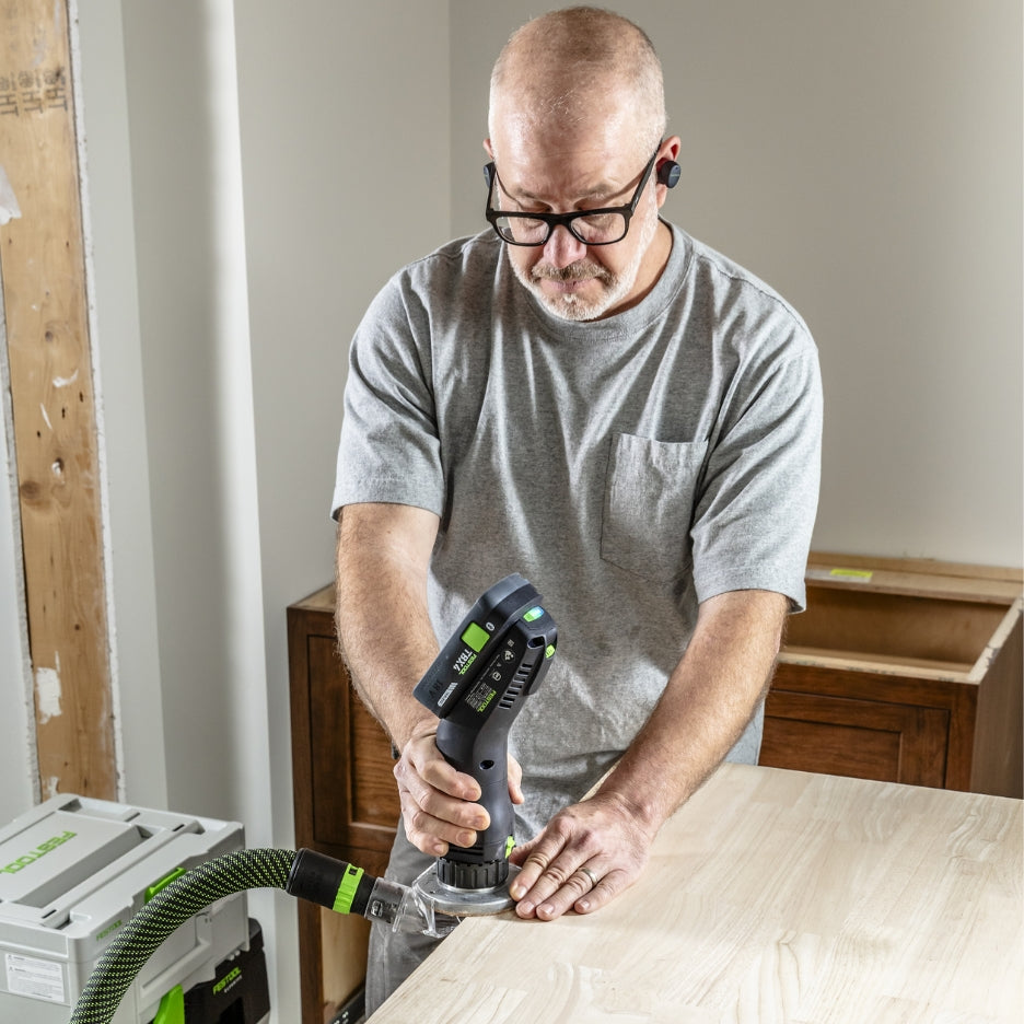 Man using Festool Cordless Edge Trimming Router OFKC 500 R3 EB-Basic on a wooden surface in a workshop setting