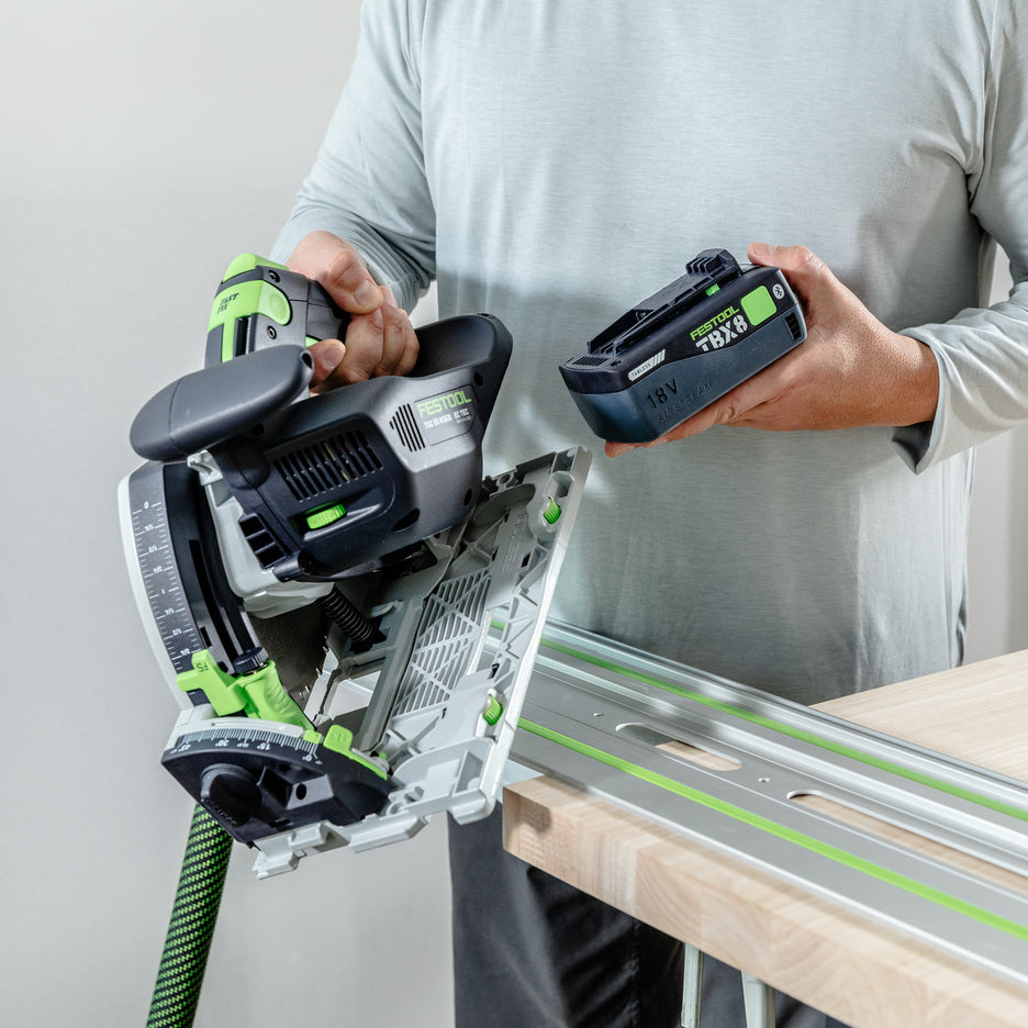 Man holds Festool TSC 55 KS in one hand and TBX8 tabless battery in the other.