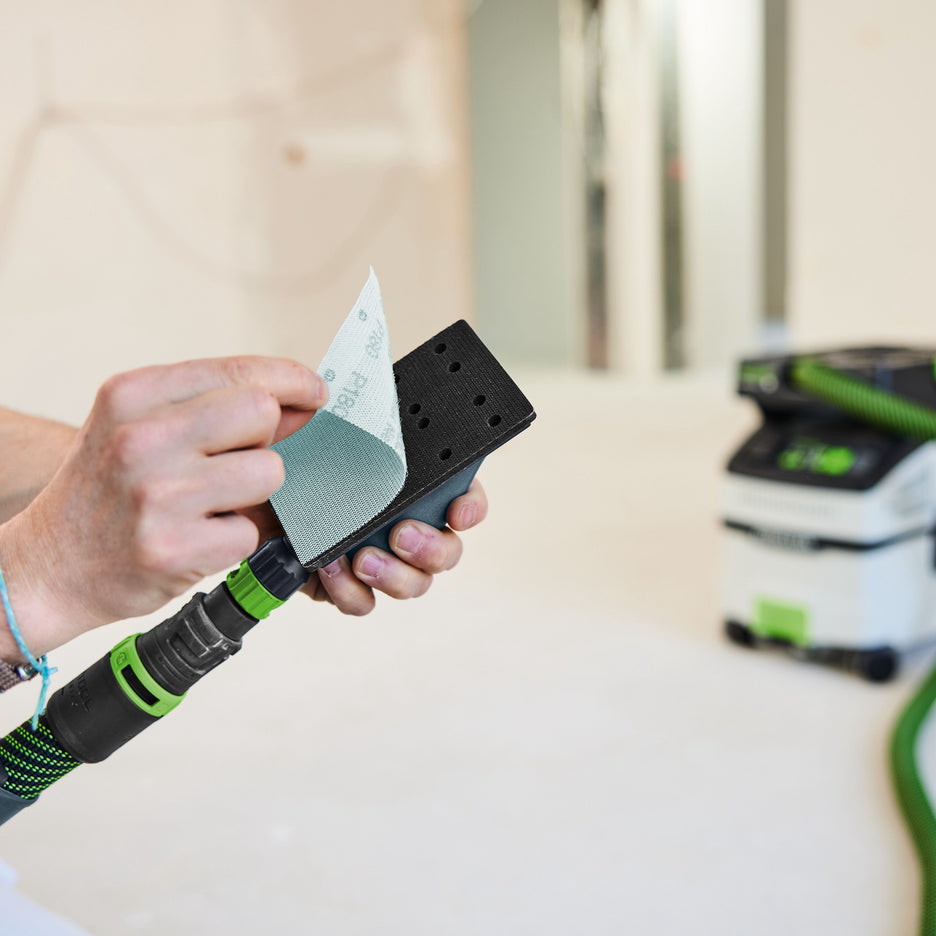 Man peels back sheet of Festool Granat Net abrasive to show the dust extraction holes in the hand sanding block.