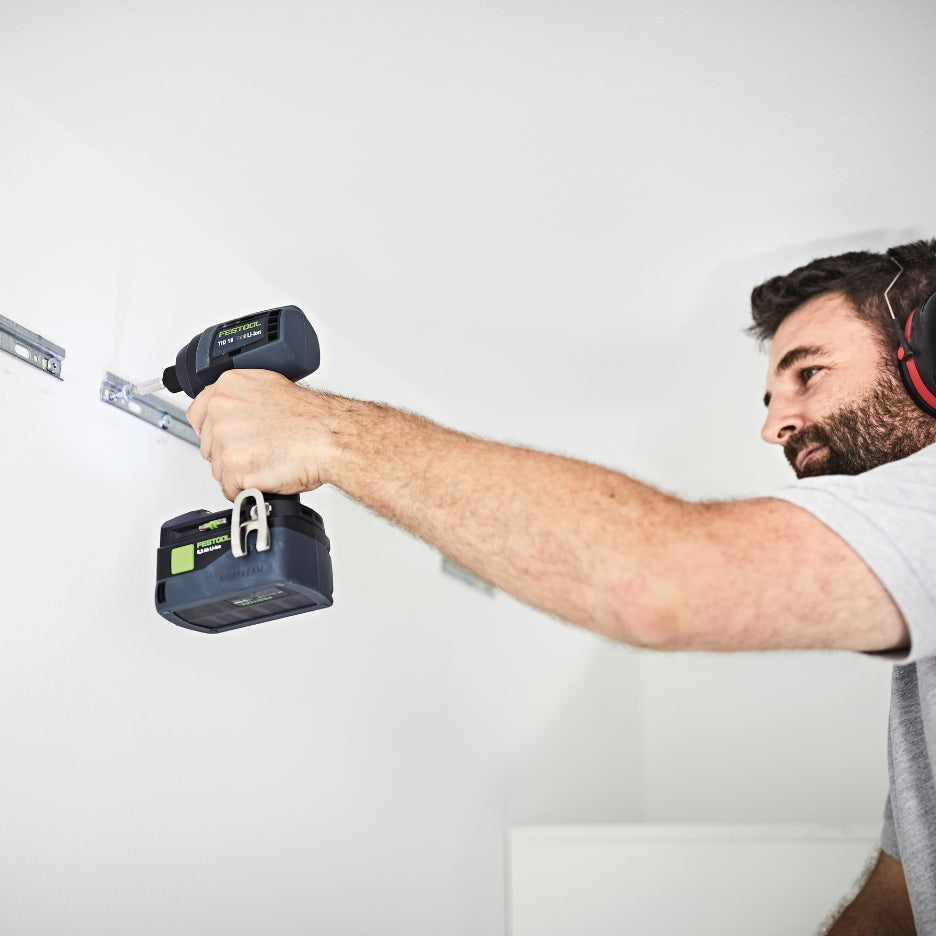 Close-up of a person using a Festool TID 18 impact driver to fasten a screw into a concrete wall.