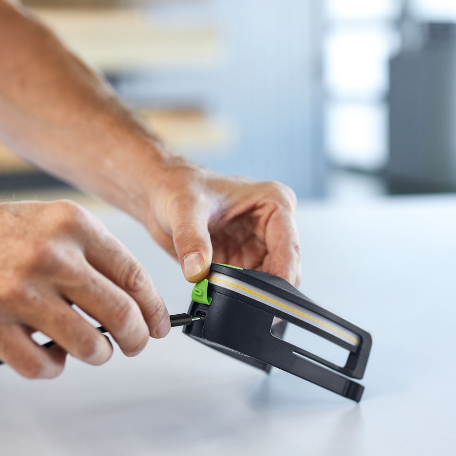 Man lifts silicone dust seal to connect USB-C charging cable on front of Festool Light Module for FestoolDTS sander.