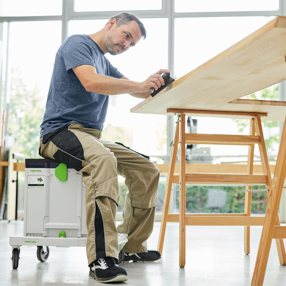 Man sits on a Seat Cushion attached to a Systainer and SYS-RB Cart as he sands the edge of a counter top on sawhorses.