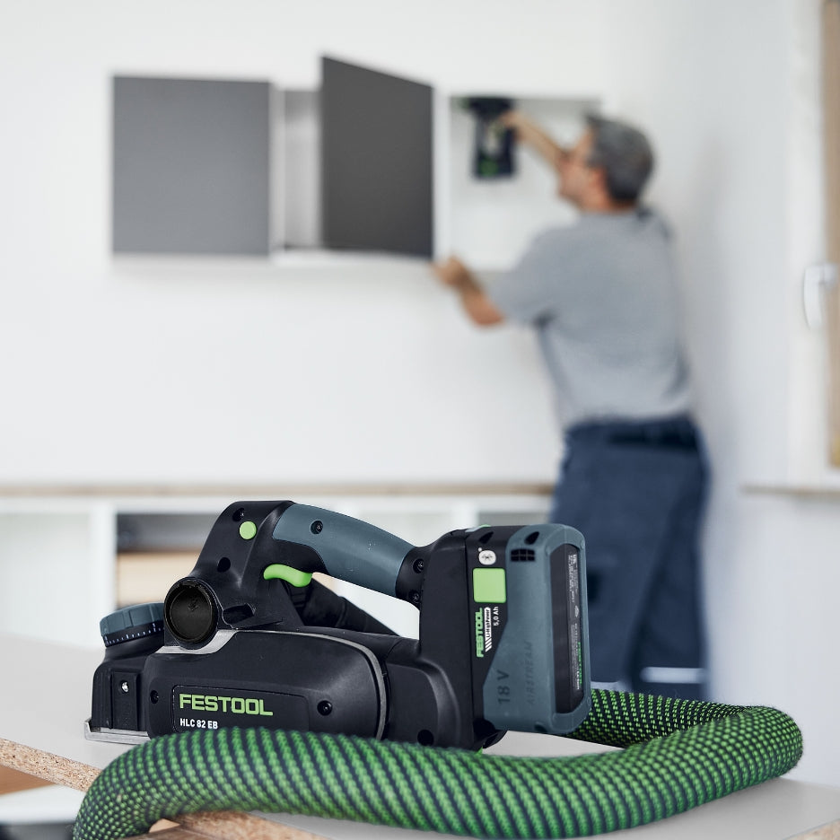 Festool power tool with Festool Tabless HighPower Battery Pack with Bluetooth and Airstream 18V 5.0Ah on a table with a blurred background of a person working.