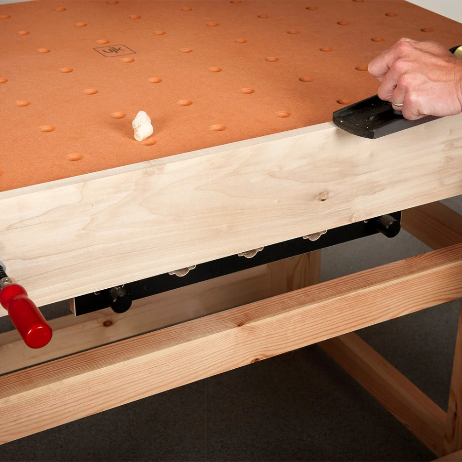 Woodworking setup with a workbench and UJK Tools HDF Valchromat Top for Parf Dogs on top, clamps, and a piece of wood.