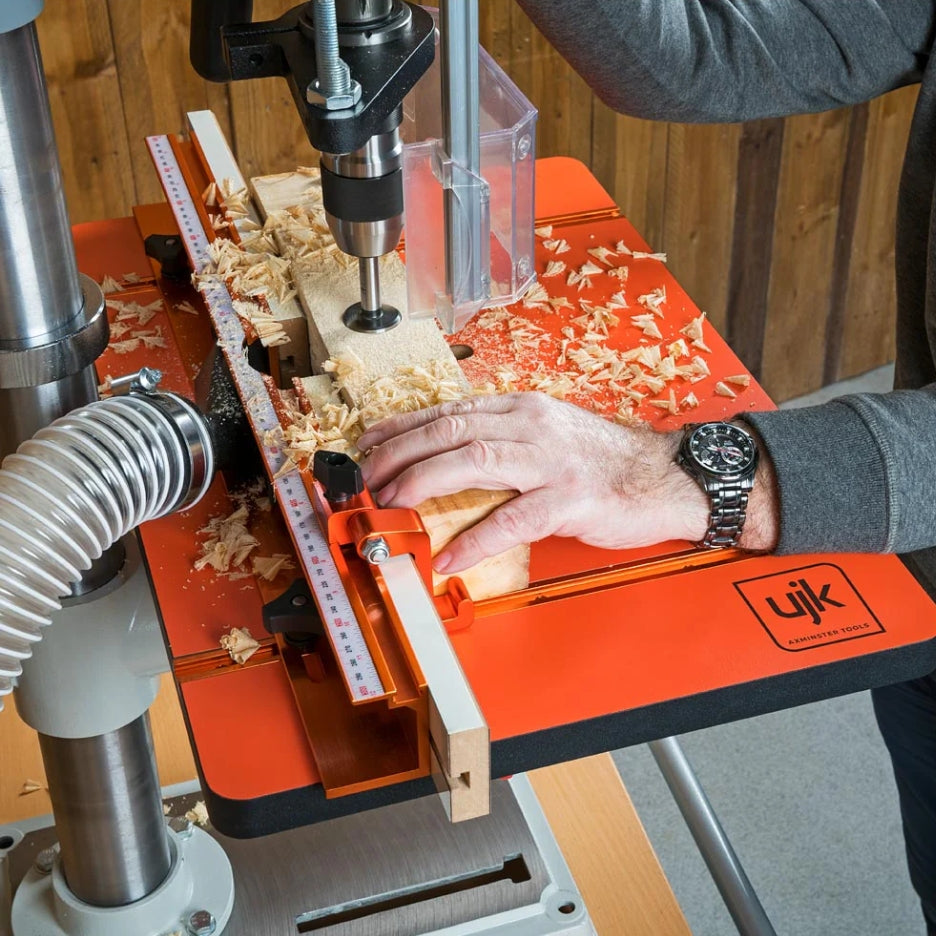 Person using UJK Tools Table and Fence for Pillar Drills with a piece of wood on a wooden workbench.