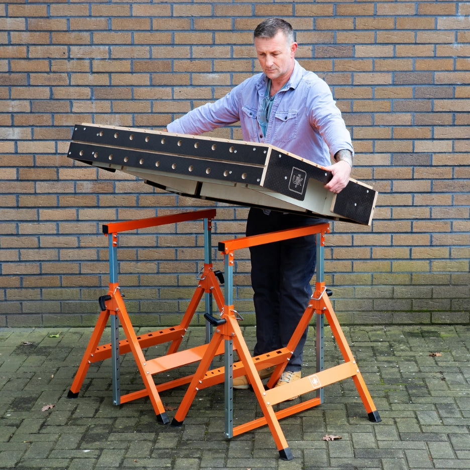 Man assembling a large wooden panel on UJK Tools Trestle against a brick wall.